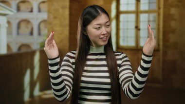 Çin 'de tarihi bir üniversite avlusunda el kol hareketi yapan, çizgili gömlek giyen, uzun saçlı, genç ve güzel, Asya kültürünü gözler önüne seren bir kadın..