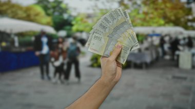 Kalabalık bir şehir sokağında, arka planda insanlarla el ele tutuşan Endonezya rupiası banknotları, gelişigüzel bir erkek varlığıyla şehir hayatı ve para birimi dinamikleri sergiliyor..