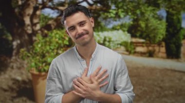 Ilık, güneşli bir günde, yemyeşil bir parkta beyaz gömlekli genç adam elleri bağlı gülümsüyor.