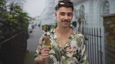 Genç İspanyol bir adam şehirde dondurma yiyor. Çiçekli gömlek ve güneş gözlüğü takıyor. Açık havada neşeli bir turist havasını kucaklıyor..