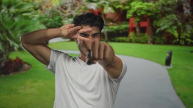 Gülümseyen adam, parktaki kıvrımlı yolda, yemyeşil güneşli yolda parmağını kameraya doğrultuyor; nişan bağlantısı güven daveti.