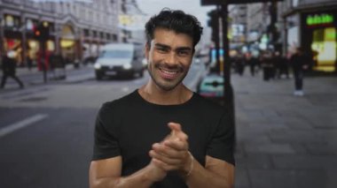 Mağazalar ve gün ışığında geçen araçlarla dolu kalabalık şehir caddesinde el çırpan adam;.