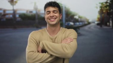 Kolları olan bir adam kalabalık bir şehir caddesini sıkıca geçerken genç bir İspanyol açık hava adamı kameraya kendinden emin bir şekilde gülümsüyor..