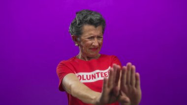 Gri saçlı, kırmızı gönüllü tişört giyen son sınıf öğrencisi kadın canlı mor arka planda duruyor..