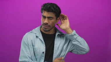Genç Hispanik adam stüdyo ortamında mor arka plana karşı el ele tutuşurken başını hafifçe eğ; merak.
