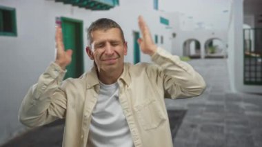 Dışarıdaki bir sokakta kulakları tıkayan bir adam, Avrupa 'nın güneşli bir köyünde endişeli bir ifadeye sahip beyaz binalarla çevrili stres ya da hayal kırıklığı gösteriyor..