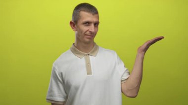 Beyaz gömlekli beyaz adam, canlı sarı duvara karşı elini uzatarak hareketlerini sergiliyor, stüdyo ortamında izole edilmiş, sunum ve pozitifliği vurguluyor..