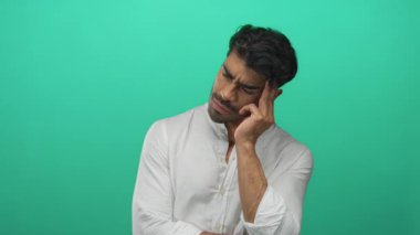 İnsan, yeşil stüdyo alanında yumuşak yönlü aydınlatma ile düşünceli bir şekilde çenesine parmak uçlarına basar; karışıklık.