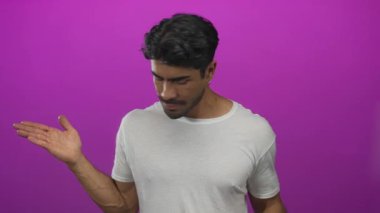 Genç İspanyol adam avuçlarını ve kollarını kaldırarak omuz silker ve parlak mor bir stüdyo görüntüsüyle başını eğer; belirsizlik.
