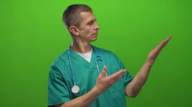 Steteskoplu doktor üniformalı bir adam yeşil arka plana el uzatıyor. Profesyonel bir tıbbi ortamda bir şeyler sunuyor..