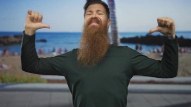 Sakallı bir adam, açık ağızlı, parlak güneş ışığı altında sahile bakan bir adamı geri çeviriyor..