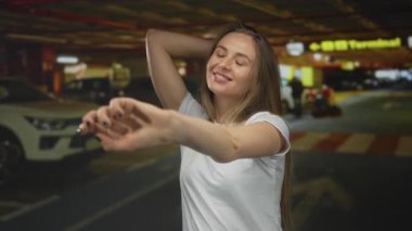 Kapalı bir otoparkta gülümseyen bir kadın, canlı arka planda, rahat bir stil sergiliyor ve neşeli bir ifade sergiliyor, modern kentsel yaşam tarzını ön plana çıkarıyor..