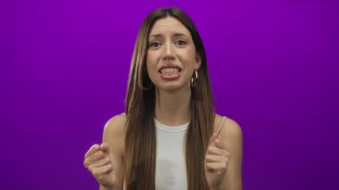 Genç İspanyol kadın stüdyo ortamında yumruklarını sıkar ve açık ağızlı kaşlarını kaldırır..