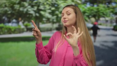 Rahat bir ifadeyle canlı yeşil bir parkta güneşli bir günün sakin, açık hava ortamını gösterirken iyi bir işaret veren bir kadın..