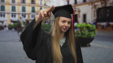 Mezuniyet üniformalı, açık hava seremonisi sırasında sokaklarda gülümseyen akademik başarı ve başarıyı temsil eden beyaz bir kadın..