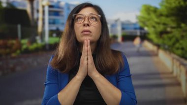 Orta yaşlı İspanyol kadın sokakta dua jestinde birbirine bastırılmış avuç içli gözlük takıyor..