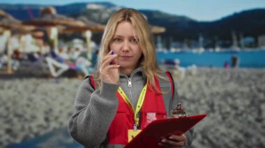 Genç gönüllü bir kadın, deniz kıyısındaki bir panoda, arka planda dağlar ve denizle birlikte açık hava aktiviteleri ve toplumsal katılımla ilgili şeyler yazıyor..