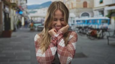 Sarışın kadın, Avrupa 'da bir şehir caddesinde parlak bir gülümsemeyle ellerini yanaklarına bastırır; neşe, neşe, neşe, neşe, neşe, huzur.