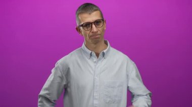 Gözlüklü ve çizgili tişörtlü bir adam göğsünde canlı pembe bir arkaplanı işaret ediyor. Merakını ya da entrikalarını izole bir ortamda ifade ediyor..