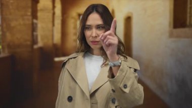 Trençkotlu genç İspanyol kadın, eski üniversite koridorunda odaklanma ve kararlılıkla el kol hareketi yapıyor..