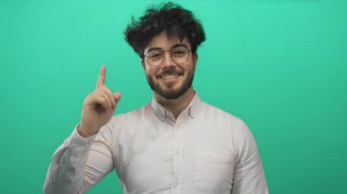 Sakallı genç adam yeşil bir arka plana karşı yukarıya doğru bakıyor, merak ve pozitiflik yayıyor..