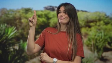 Yeşilli yeşil bir park ortamında, kırmızı tişört giyen, dışa dönük, dışa dönük, onaylanmamış hareketler yapan bir kadın..