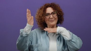 Mor arka planda poz veren, orta yaşlı esmer, gözlüklü ve rahat gömlekli, yaratıcı ve odaklı bir kadın..