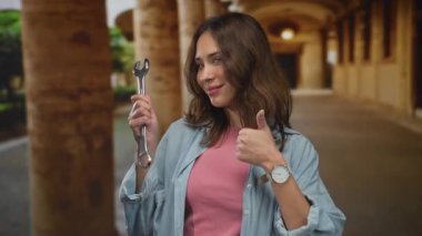 Şehrin dışında ingiliz anahtarı tutan genç İspanyol kadın kendine güvenen bir gülümsemeyle başparmağını kaldırıyor.
