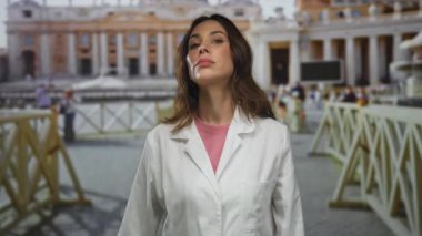 San Pedro Meydanı 'nda dikilen genç İspanyol kadın Vatikan' ın arka planına karşı beyaz önlüklü, insan ve mimari manzaralı..