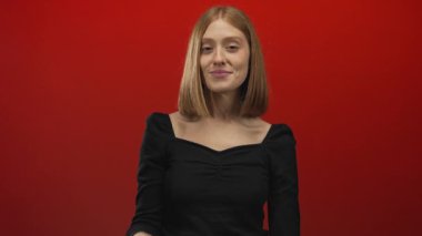 İzole edilmiş kırmızı bir stüdyo duvarının önünde sessiz kalmak için parmaklar dudaklara genç sarışın kadın; gizlilik sessizlik sessizlik sessizlik sessizlik sessizlik.