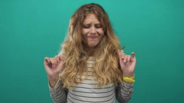 Stüdyoda endişeli bir ifadeyle el kaldıran bir kadın tasviri. Yeşil bir arka planla zıt duran çizgili bir saatin altında gevşek sarı saçlar sergiliyor..