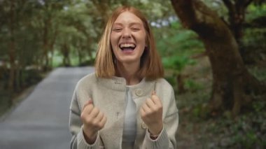 Huzurlu bir açık hava parkında gülümseyen bir kadın yemyeşil ağaçlar ve sakin doğal bir arka plan ile neşeli ve ferahlatıcı bir atmosfer yaratıyor..