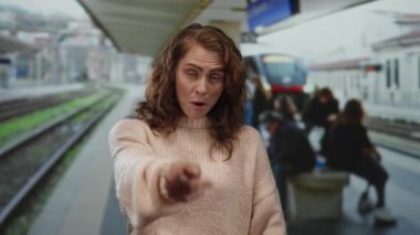 Tren istasyonunda arka planı bulanık gülümseyen, süveter giyen, dışarıda tren ve insanlarla çevrili neşeli bir seyahat anını tasvir eden bir kadın..