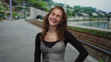 Tren istasyonundaki kadın, arka planda demiryolu manzarasıyla mutlu bir şekilde gözlerini kapatıyor, genç neşe ve seyahat beklentisinin somutlaştırılmış hali..