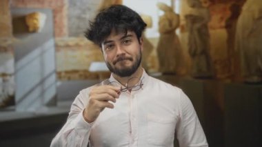 Müzede gülümseyen sakallı genç bir adam. Arka planda heykeller var. İçeride neşeli ve rahat bir atmosfer sergiliyor..