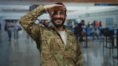 Askeri üniformalı İspanyol bir adam hareketli bir havaalanı terminalinde selamlıyor. 1 numaralı terminaldeki kalabalık arasında bir saygı anı yakalıyor..