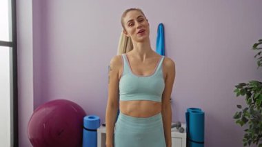 Sarışın, beyaz bir kadın spor salonunda karnını açmak için kollarını uzatıyor..