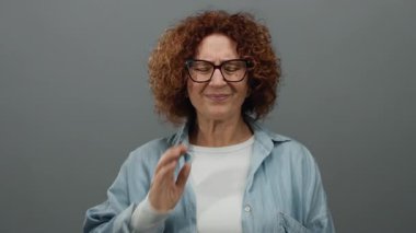 Yüzü gri duvara dönük, acı çeken, orta yaşlı, gözlüklü, kıvırcık saçlı, günlük gömlekli, izole edilmiş arka planda rahatsızlık gösteren bir kadın..