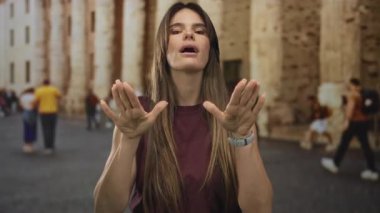Şehir sokaklarında sakinlik için el kol hareketi yapan, bulanık kalabalığın ve tarihi mimarinin ortasında İspanyol genç bir kadını gösteren bir kadın..
