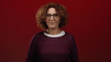 Esmer kadın, kültürel ifadelerini sergileyen canlı kırmızı duvara karşı sessizliğini gösteriyor..