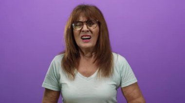 Göğsünü tutan kadın, mor duvara karşı rahatsızlığını dile getiriyor. Duygularını ve sağlık sorunlarını ifade ediyor..