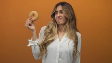 Sarışın kadın, parmak ve başparmağıyla donut tutarken ve stüdyoda el kaldırırken tiksindirici yüz ifadesi takınıyor..