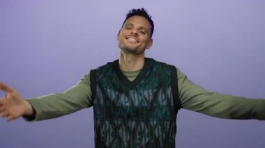 Genç adam, izole edilmiş mor bir arka planda sıcaklığı ve kendini sevgiyi yansıtan günlük giysiler içinde gülümseyerek kendini kucaklıyor..