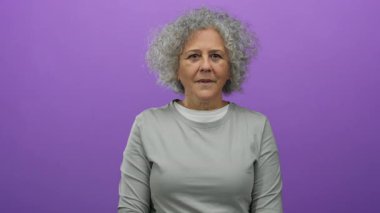 Mor arka planda gri saçlı orta yaşlı bir kadın günlük kıyafetleriyle sürpriz yapıyor..