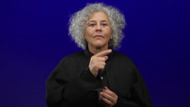 Gri saçlı yaşlı kadın, izole edilmiş mavi bir arka plana karşı sessizliğini koruyor. Huzur ve sükuneti iletiyor..