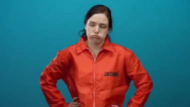 Turuncu hapishane tulumu giymiş bir kadın mavi bir arka plana karşı duruyor. Sıkıntısını ve hayal kırıklığını ifade ediyor. Gözleri kapalı ve kolları çapraz..