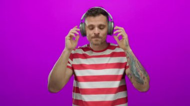 Kulaklıkla gülümseyen bir adam, parlak pembe bir arkaplan karşısında çizgili bir tişörtle olumlu duygu ve zevk ifade ederek başparmak kaldırır..