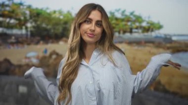 Genç sarışın kadın yüzünü kumsalda gülümseyerek, esinti yaparak saçlarını ve rahat omuzlarını sallayarak gösterir; rahatlama mutluluğu.