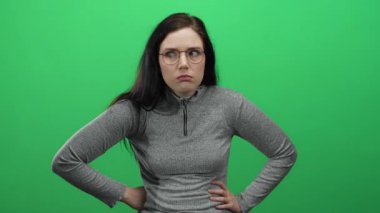 Gözlüklü kadın, parlak yeşil bir arka plana karşı ifadeler sergiliyor gri bir kazak giyiyor duyguları ve doğal güzelliği yakalıyor.