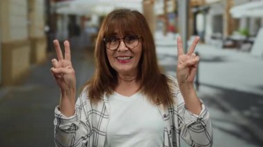 Kıdemli İspanyol kadın gülerek ve iki eliyle barış işareti yaparak şehrin ortasında gündüz vakti dikiliyordu..